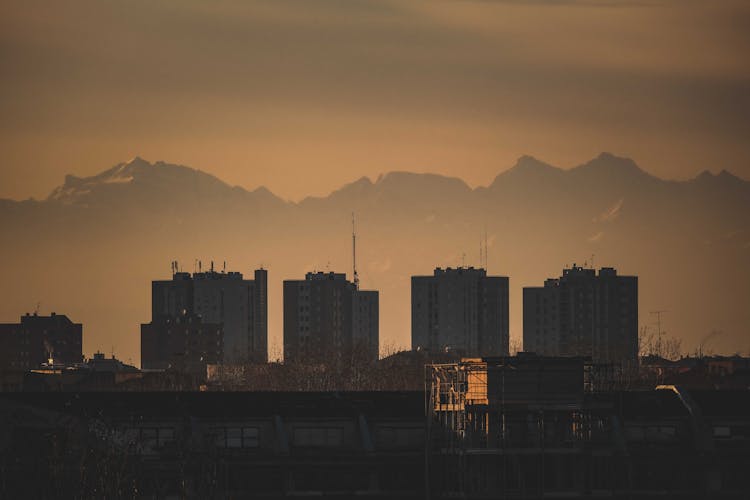 Silhouetted Buildings In City And Mountains In Distance At Sunset 