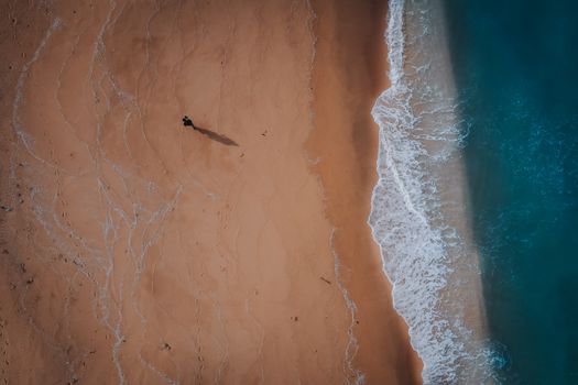 Aerial view of a lone person walking along the serene Marang beach in Terengganu, Malaysia with gentle waves.