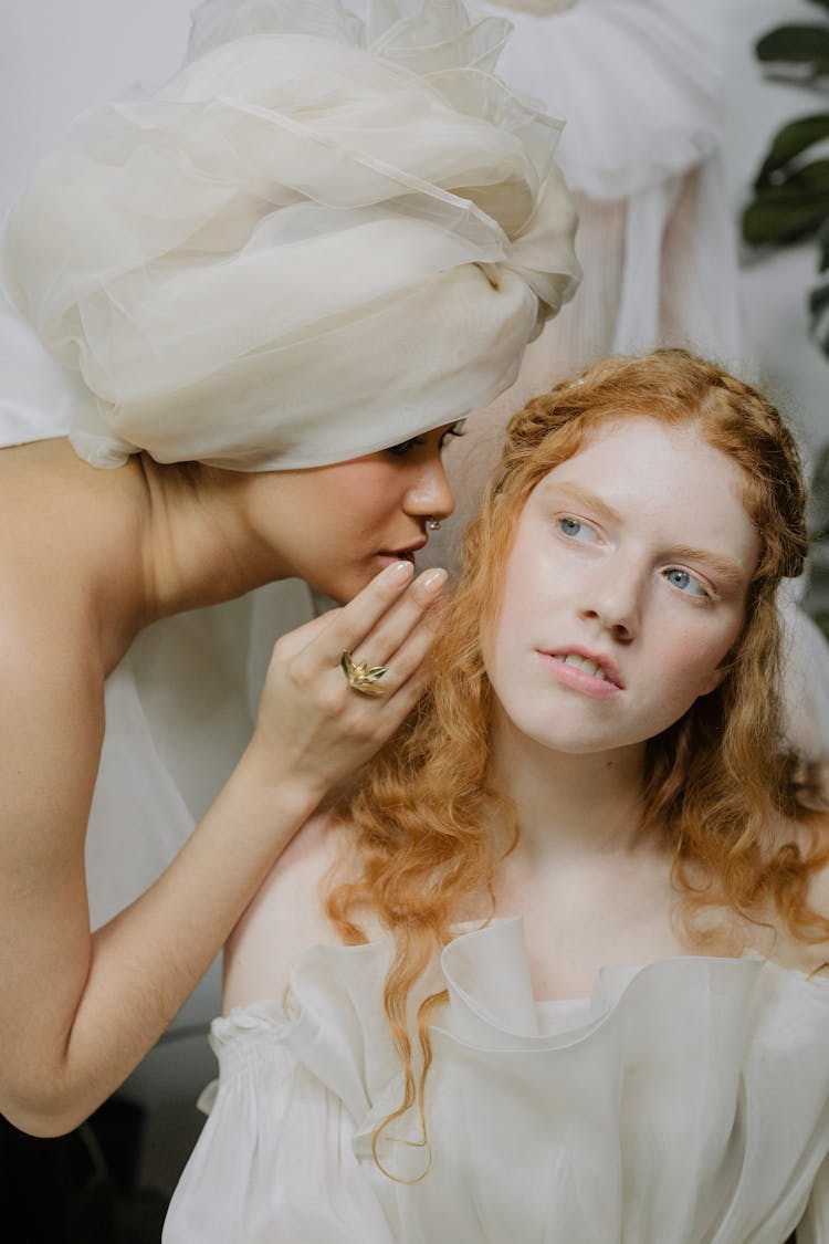 Woman Wearing A Headwrap Whispering Into Another Woman's Ear