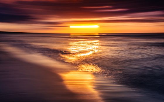 A stunning long exposure capture of a colorful sunset over ocean waves, creating a dramatic seascape reflection.