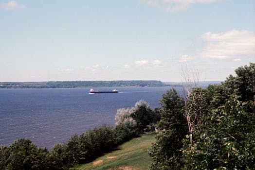 Serene landscape of St. Lawrence River with a cargo ship passing by lush greenery in Quebec City.