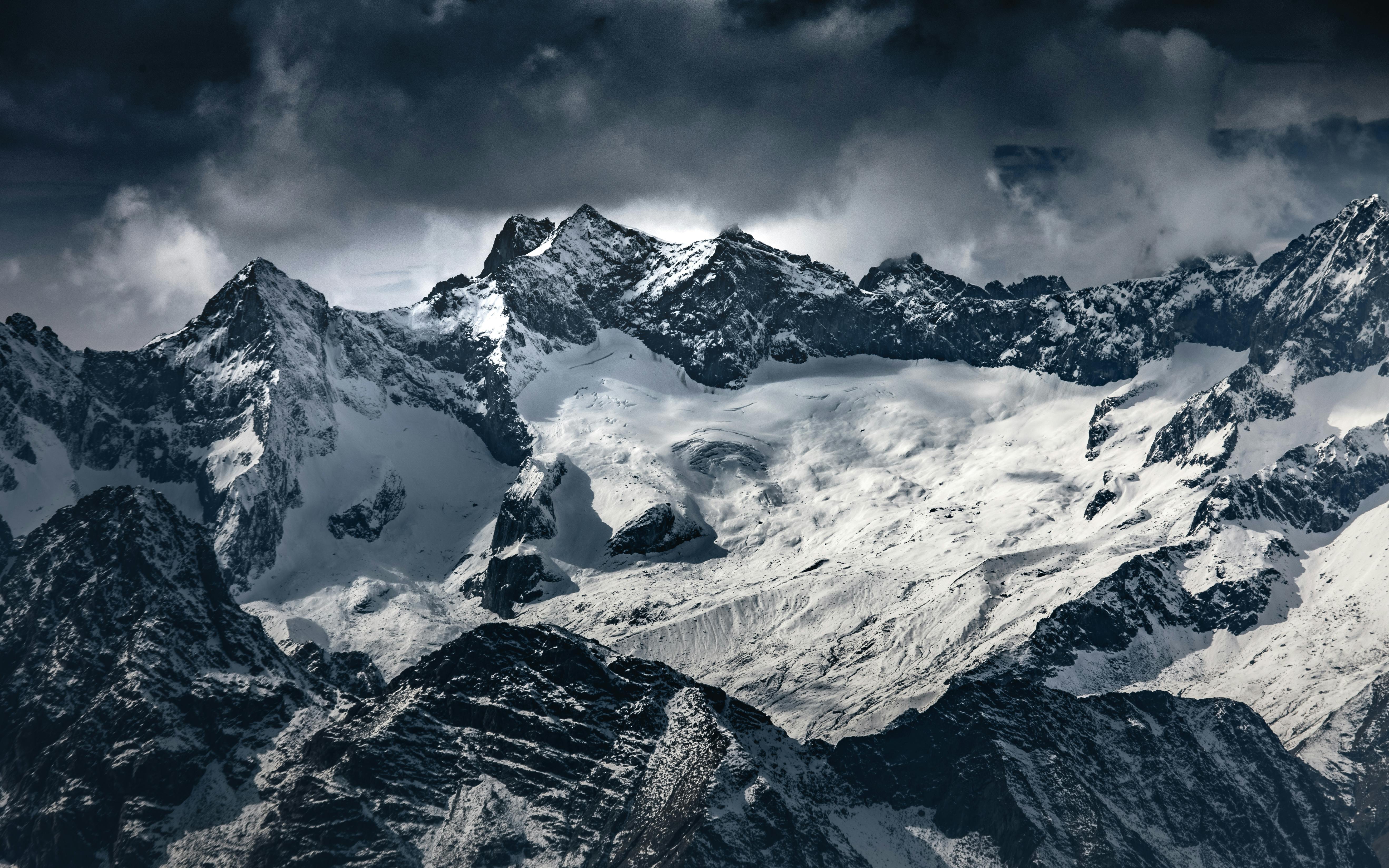 Majestic view of the snow-capped Italian Alps with dramatic clouds overhead, showcasing winter's beauty.