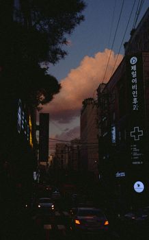 Dusk settles over a lively street in Seoul, South Korea, highlighted by bustling traffic and illuminated signs.
