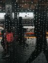 Silhouettes of anonymous passengers with carriage walking on asphalt platform of railway station through wet window with drops of rain at night