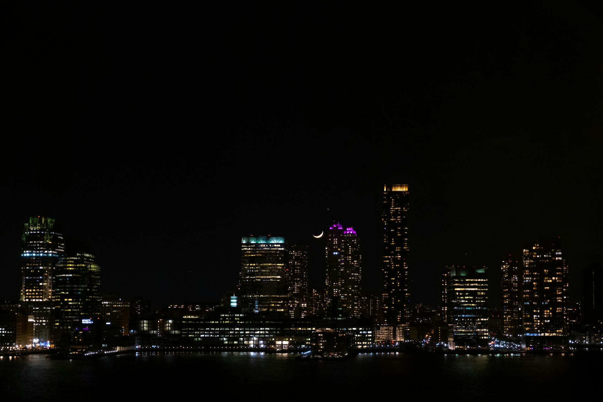 Stunning nighttime view of New York City skyline with illuminated skyscrapers and crescent moon.
