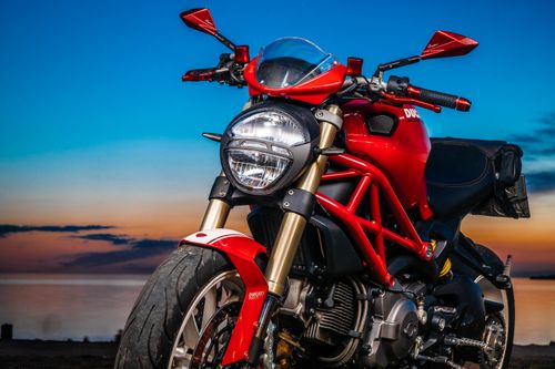 Free A striking red Ducati motorcycle parked against a colorful twilight sky by the seaside. Stock Photo