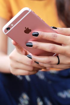 A woman with black nail polish holding a rose gold smartphone, showcasing a modern lifestyle.
