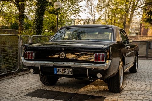Free Rear view of a classic black Ford Mustang parked on cobblestone, surrounded by greenery in a peaceful setting. Stock Photo