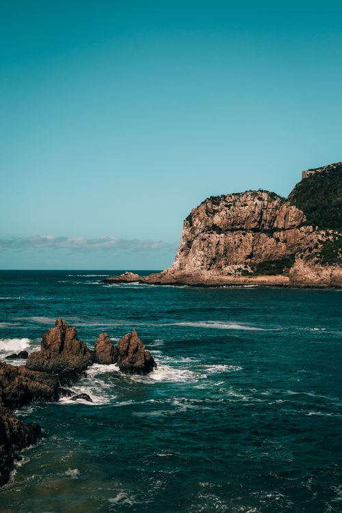 Free Majestic coastal rock formations meet the ocean under a clear sky, offering a scenic view. Stock Photo