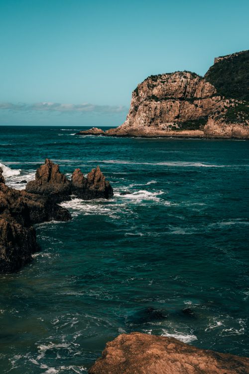 Free A stunning view of rugged cliffs by the ocean under a clear blue sky. Stock Photo