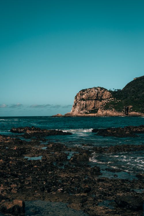 Free Vertical shot of a dramatic seascape with a rocky formation under clear blue skies and ocean waves. Stock Photo