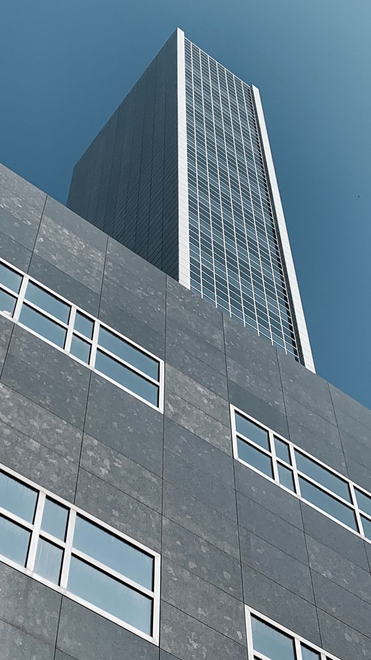 Laag perspectief van een moderne wolkenkrabber in Amsterdam, met strakke architectuur tegen een heldere blauwe lucht.