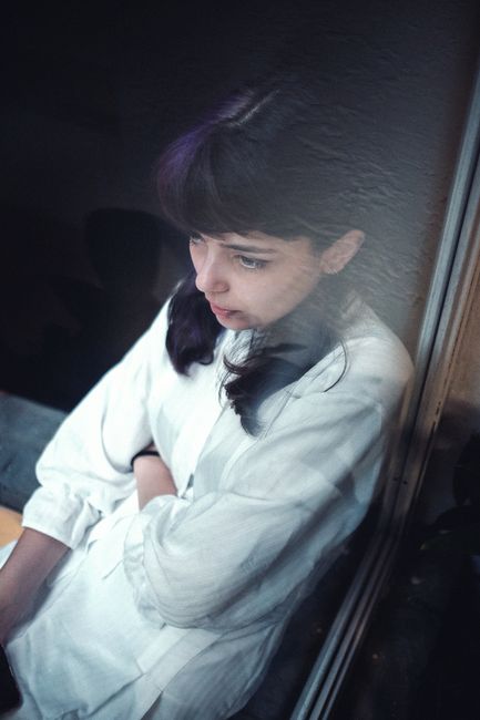 From above of gentle teenager pondering and dreaming while leaning on glass of window