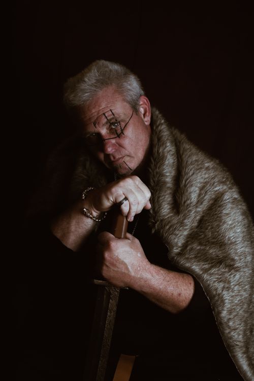 Free Elderly man with gray hair holds sword in a dramatic, moody studio portrait. Stock Photo