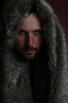 Portrait of a man in a fur hood with a serious expression, captured in a studio setting.