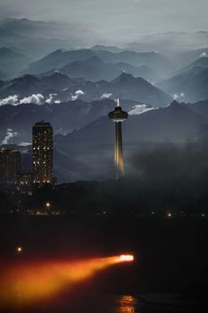 Scenic cityscape with skyscrapers and a tower with mountains and fog at twilight.
