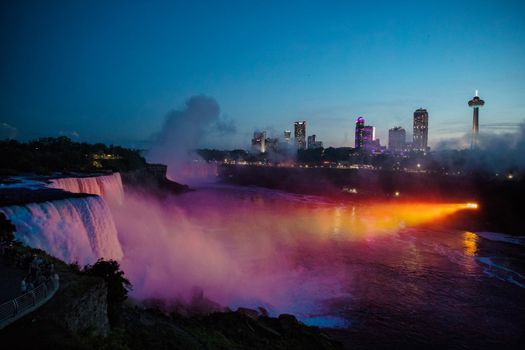 Dramatic night view of Niagara Falls with colorful city lights and mist.
