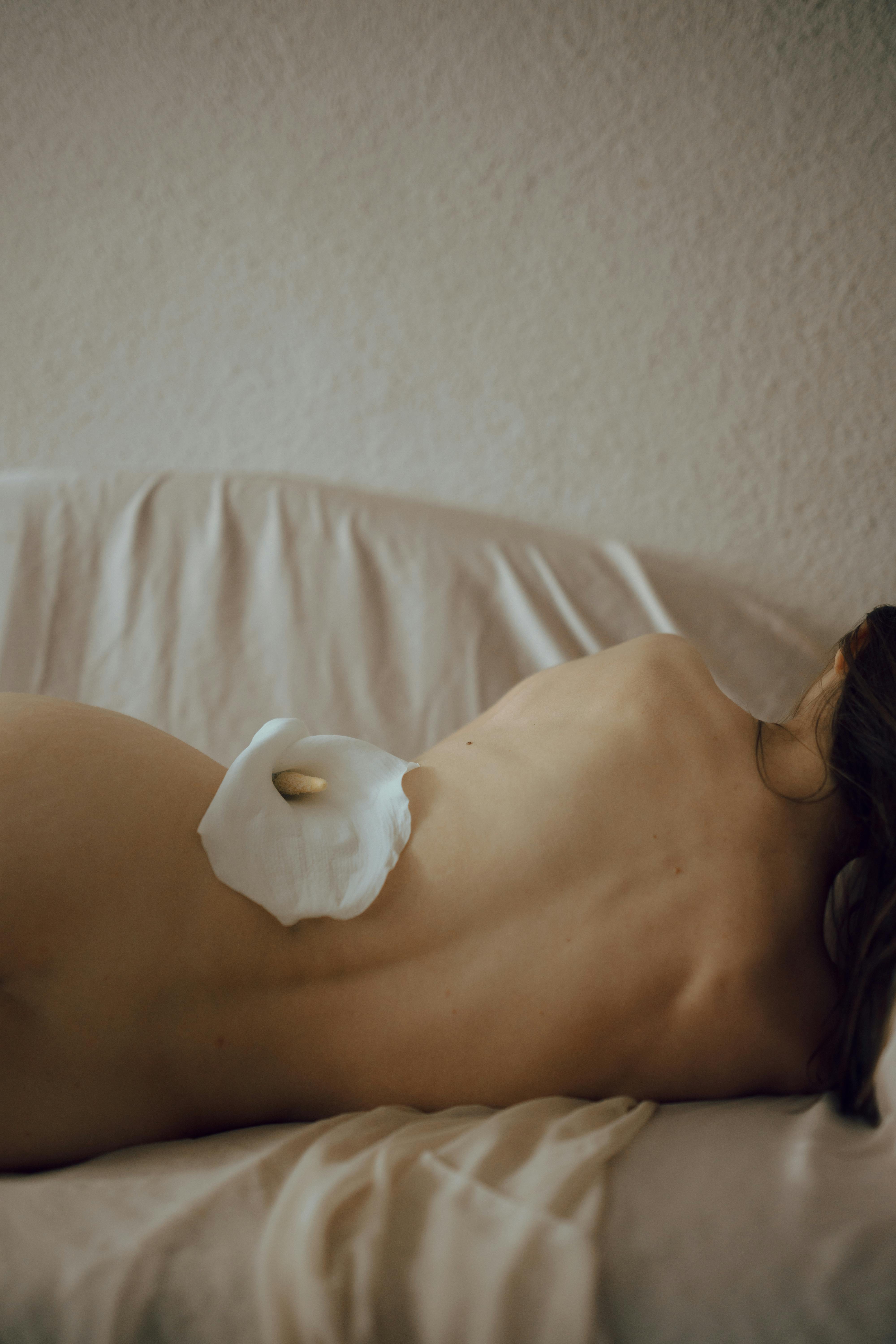 unrecognizable woman lying on couch with delicate flower on naked body