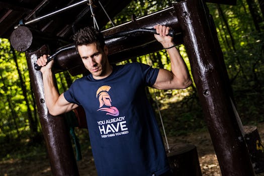 A man in a motivational t-shirt using an outdoor gym in a forest setting.
