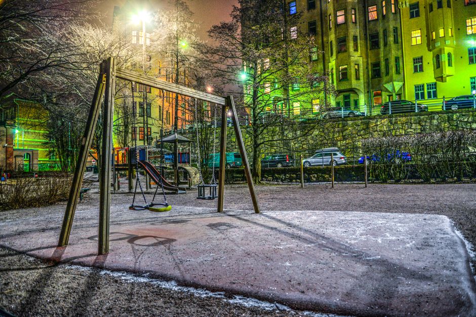 A nighttime view of an empty playground surrounded by illuminated urban buildings.