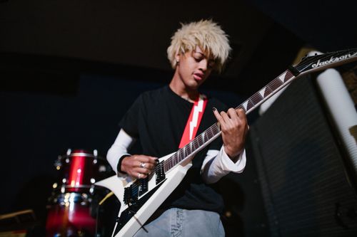 Free Energetic young guitarist playing a white electric guitar in a dimly lit room. Stock Photo
