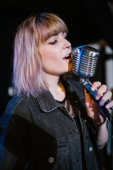 Young female singer in denim jacket singing into vintage microphone at a concert.