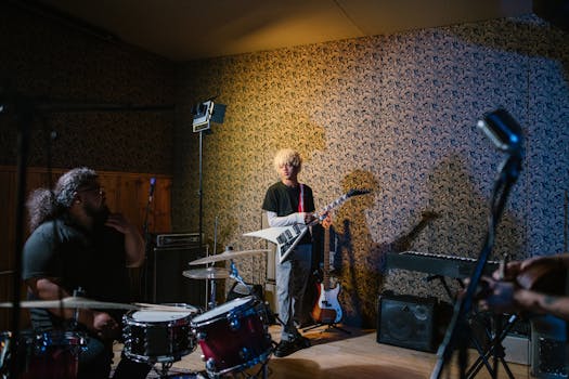 Band members rehearsing with instruments in a cozy indoor studio setting.