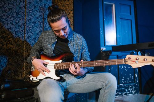 Free A young musician focuses intensely while playing an electric bass guitar in a cozy indoor setting. Stock Photo