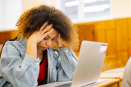 Free A young woman experiencing a headache while studying with a laptop indoors, looking stressed and overwhelmed. Stock Photo
