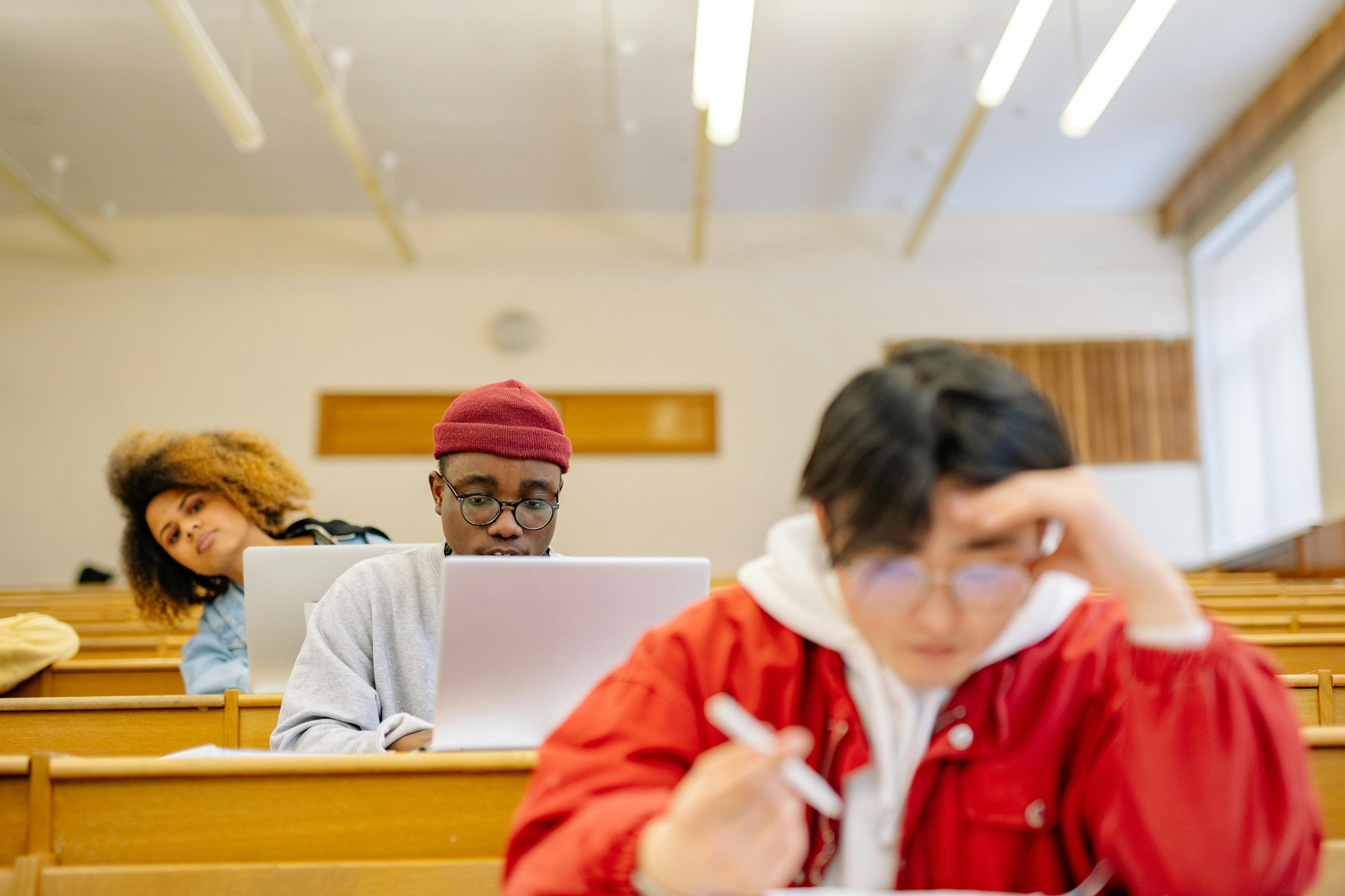 Students study with laptops and notes while seated in a university lecture hall.
