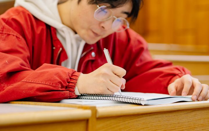 A student focused on writing notes in a lecture hall, emphasizing learning and concentration.