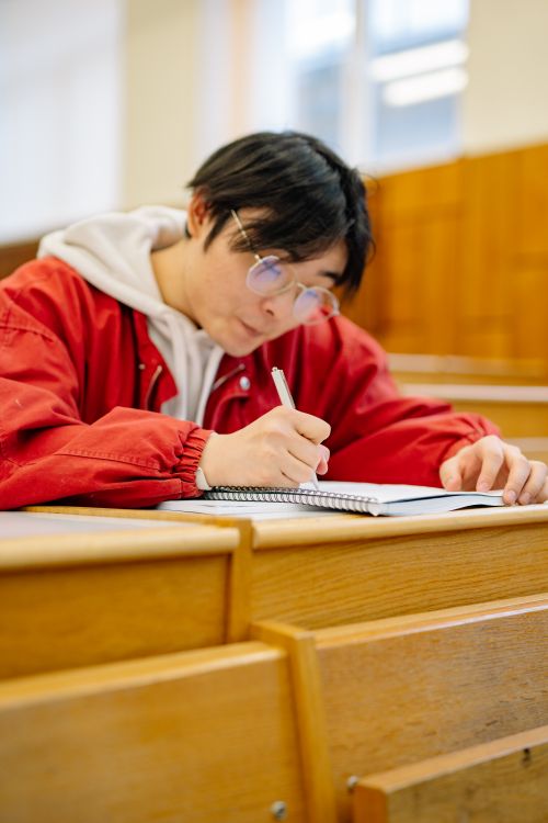 Free A student focused on writing notes in a lecture hall, emphasizing learning and concentration. Stock Photo
