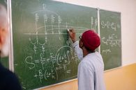 Man in Red Cap and Gray Shirt Writing on Chalk Board