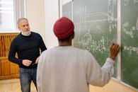 Man in Black Crew Neck Shirt and Red Cap Standing Beside Man in Gray Sweater