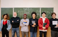 A diverse group of students and a teacher smiling in front of a chalkboard filled with formulas.