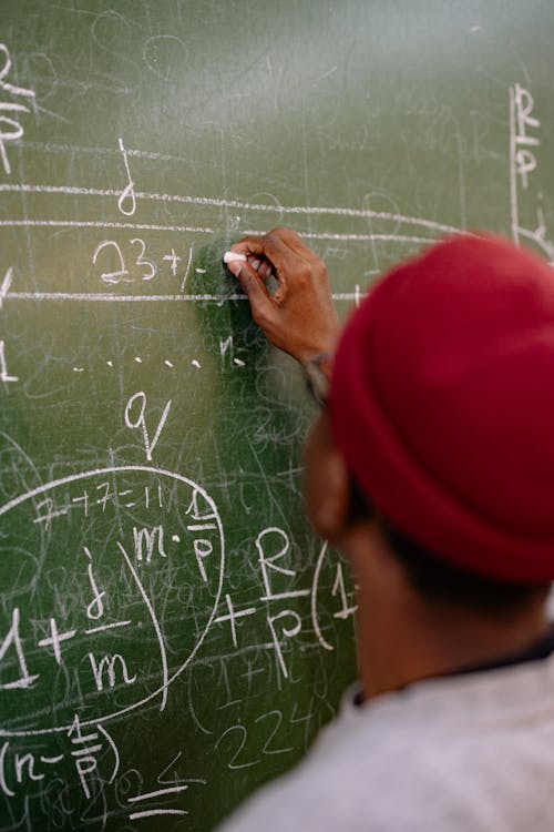 Back View of a Student Writing a Math Equation on a Blackboard 