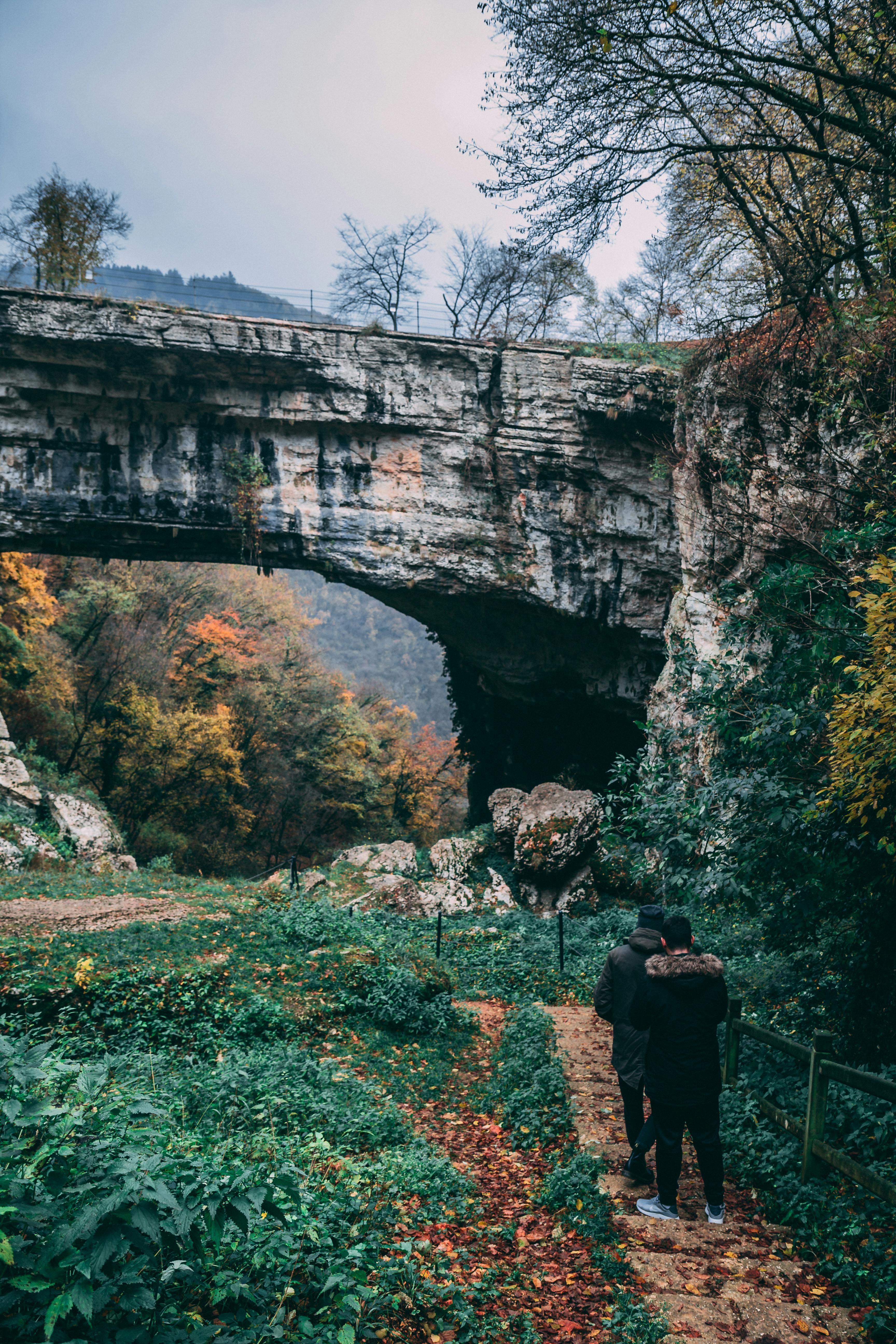 一对夫妇在郁郁葱葱的森林中，于雄伟的石桥下享受宁静的秋日散步
