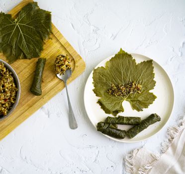 Top view of stuffed grape leaves with rice on a wooden board and white plate.