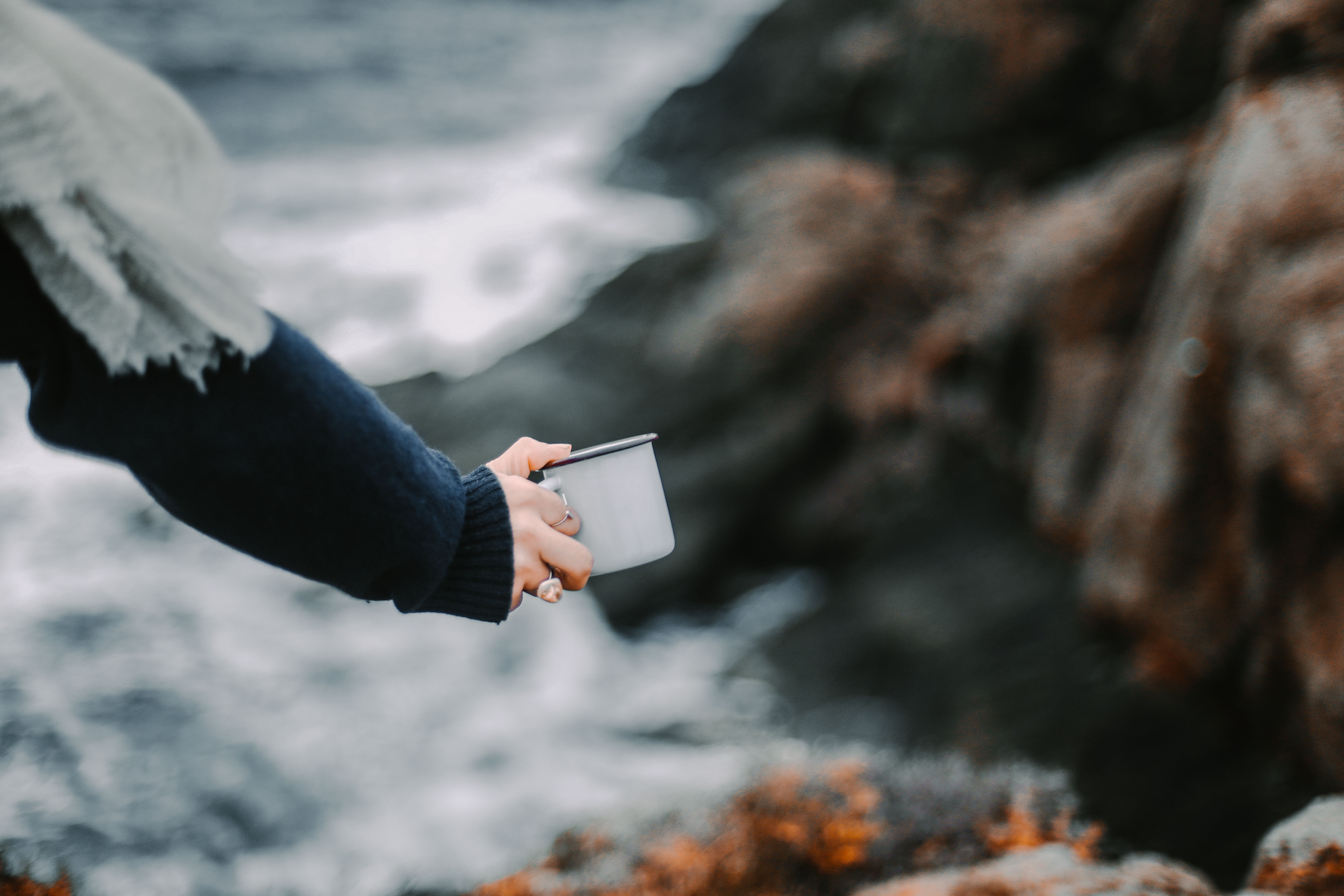 Adult holding a mug with scenic ocean background, captured outdoors.