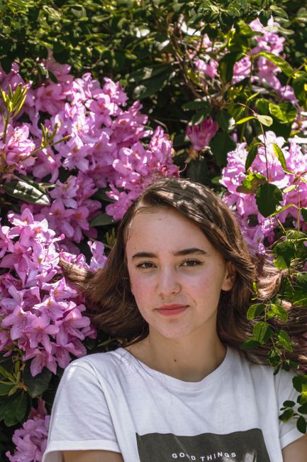 Portrait of a young woman in a garden surrounded by vibrant pink flowers and lush leaves.