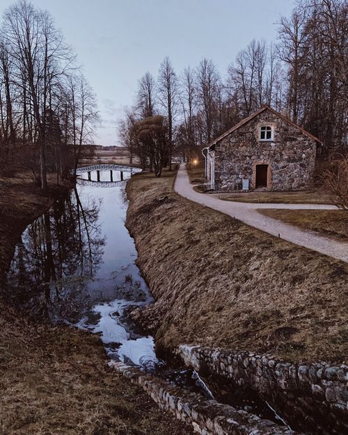 Free Idyllic stone house beside a reflective canal surrounded by leafless trees in Russia. Stock Photo
