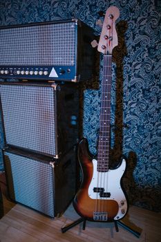 Electric bass guitar leaning against stacked amplifiers in a dimly lit studio setting.