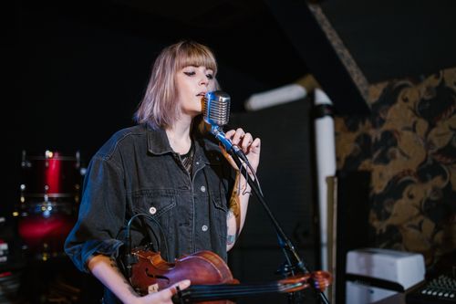 Free Woman singing while holding a violin on stage with a vintage microphone. Stock Photo