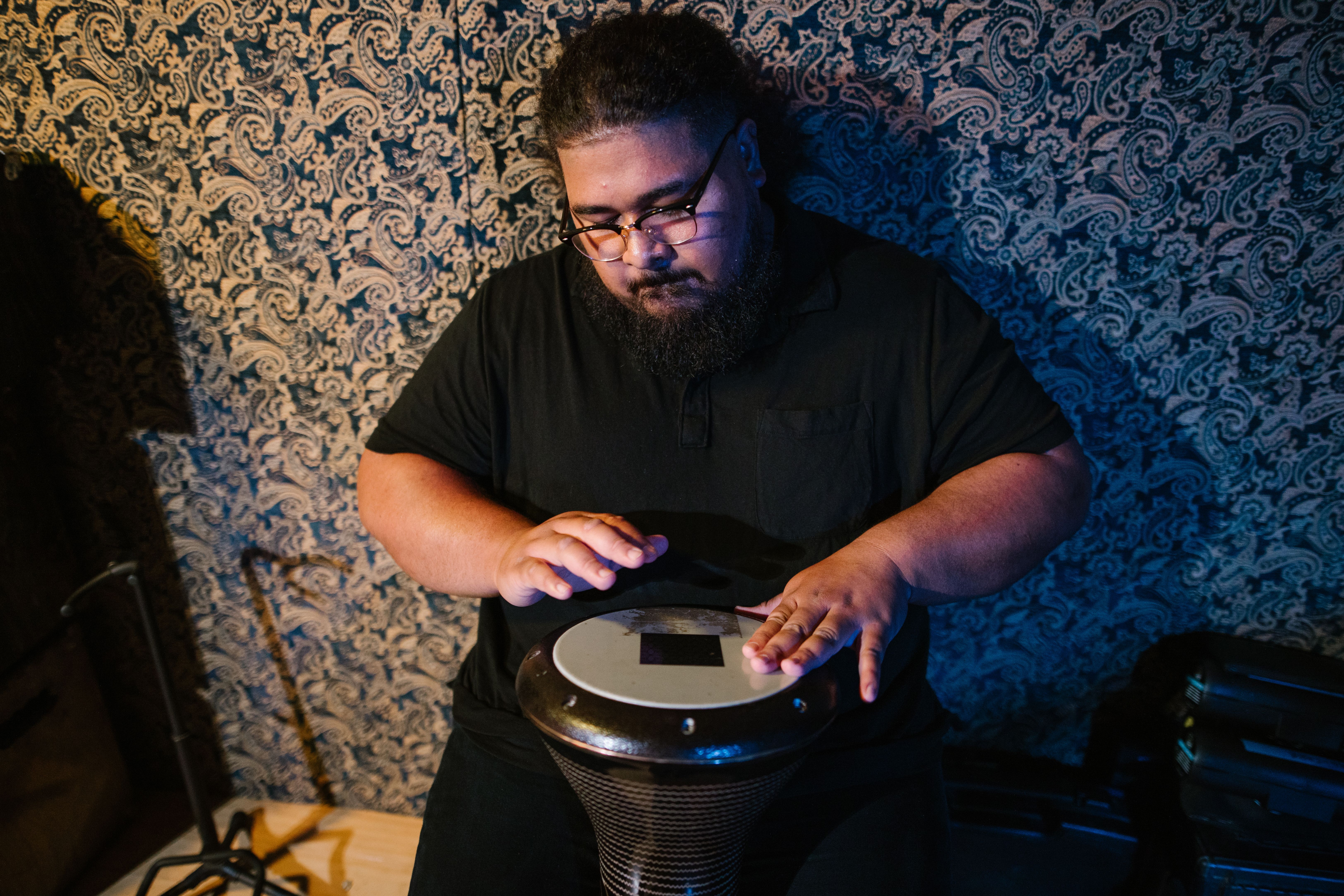 An adult musician skillfully plays a hand drum in an indoor studio setting.