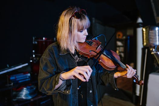 Female violinist performing indoors, wearing a denim jacket, with vintage microphone nearby.