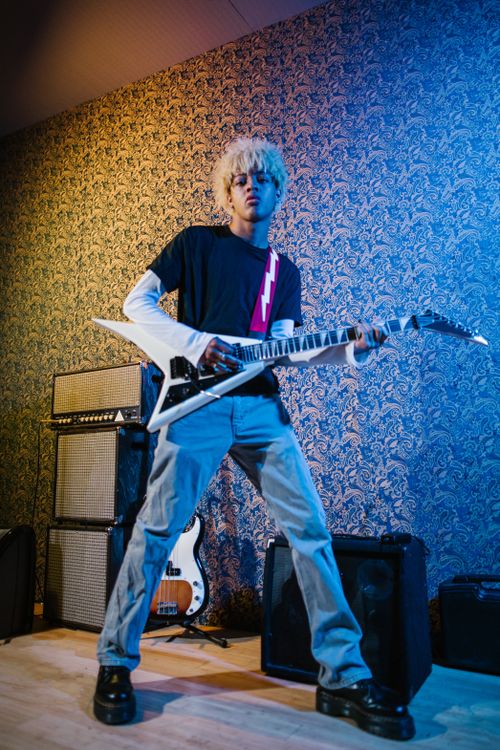 Free Energetic young guitarist playing an electric guitar indoors with a stylish backdrop. Stock Photo