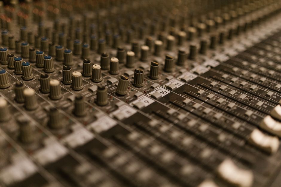 Close-up of a professional audio mixer with faders and knobs in a recording studio setting.