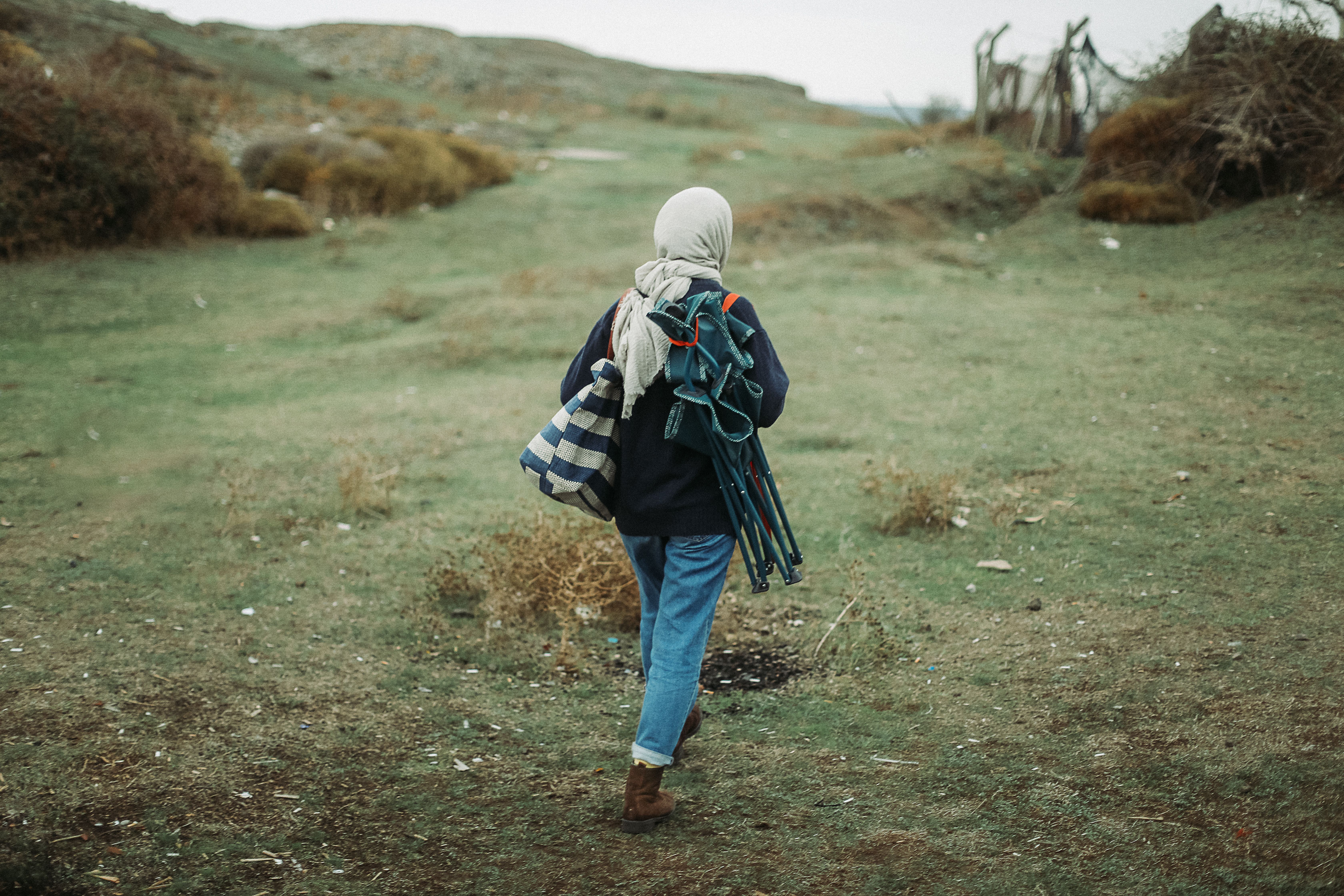 A woman with a headscarf hiking in the countryside carrying equipment. Ideal for outdoor and travel themes.