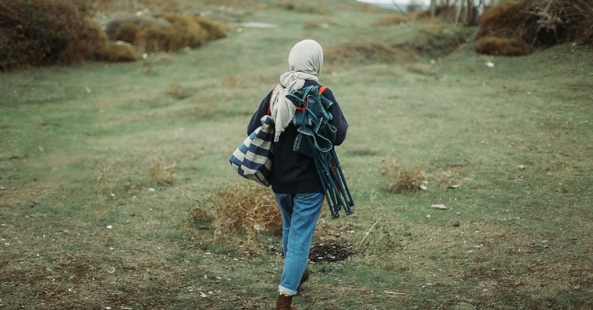 A woman with a headscarf hiking in the countryside carrying equipment. Ideal for outdoor and travel themes.