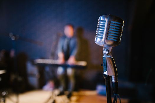 Close-up of a vintage microphone with a musician playing keyboard in the background, creating a musical atmosphere.